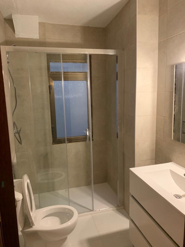 Reforma de baño con plato de ducha blanco, mampara de cristal y mueble suspendido en Etxebarri