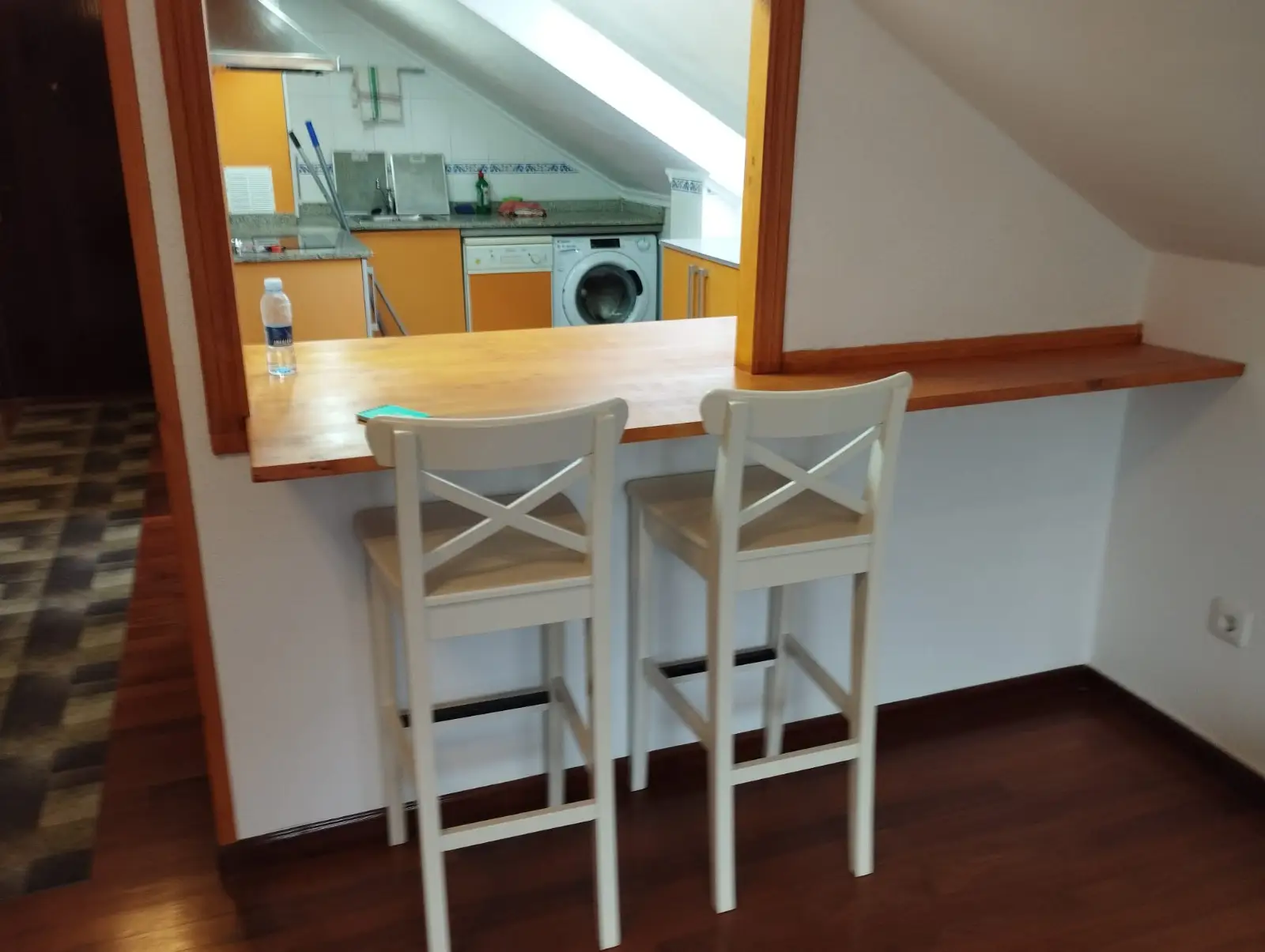 Reforma de cocina con barra de madera y taburetes blancos en un ático de Etxebarri